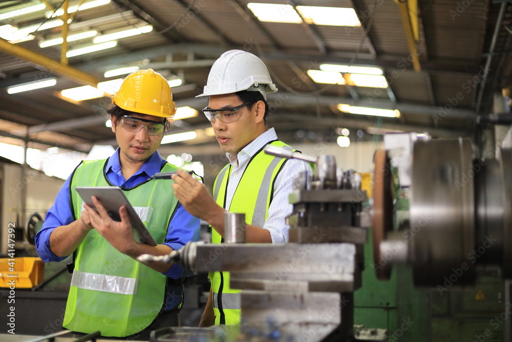 Asian engineering manager and mechanic worker in safety hard hat and reflective cloth using lathe machine inside the factory Asian engineering manager and mechanic worker in safety hard hat and reflective cloth using lathe machine inside the factory