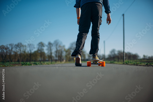 legs of man standing on skateboard on street in front of trees