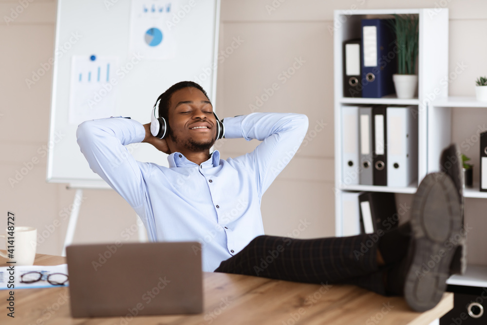 Fototapeta premium Relaxed black man employee listening to music in his office