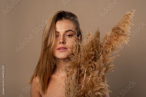 Close up beauty portrait of an attractive young topless woman with brown hair isolated over beige background, holding dried herb. Skin care concept