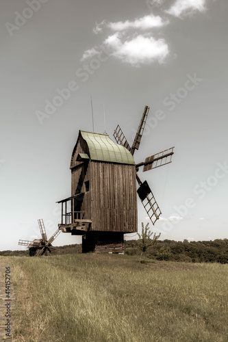 Old wodden windmill on a green meadow, field. Blue sky with white clouds. Old photo.