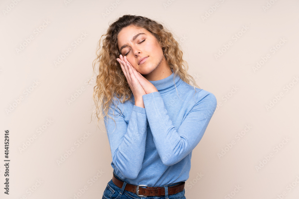Young blonde woman with curly hair wearing a turtleneck sweater isolated on beige background making sleep gesture in dorable expression Young blonde woman with curly hair wearing a turtleneck sweater isolated on beige background making sleep gesture in dorable expression