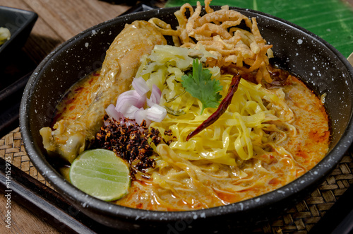 The tasty egg yellow noodle in chicken curry soup with ingredients in the bowl on wooden table. Kao Soi Kai, this is name of the traditional food of northern Thailand..