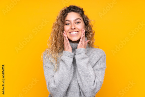 Young blonde woman with curly hair wearing a turtleneck sweater isolated on yellow background smiling with a happy and pleasant expression © luismolinero