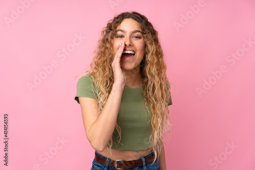 Young blonde woman with curly hair isolated on pink background shouting with mouth wide open