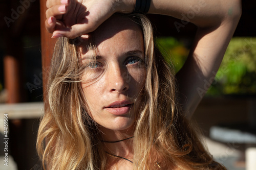 close up portrait of young beautiful blonde woman with long wavy hair and blue eyes in harsh sunlight outdoor