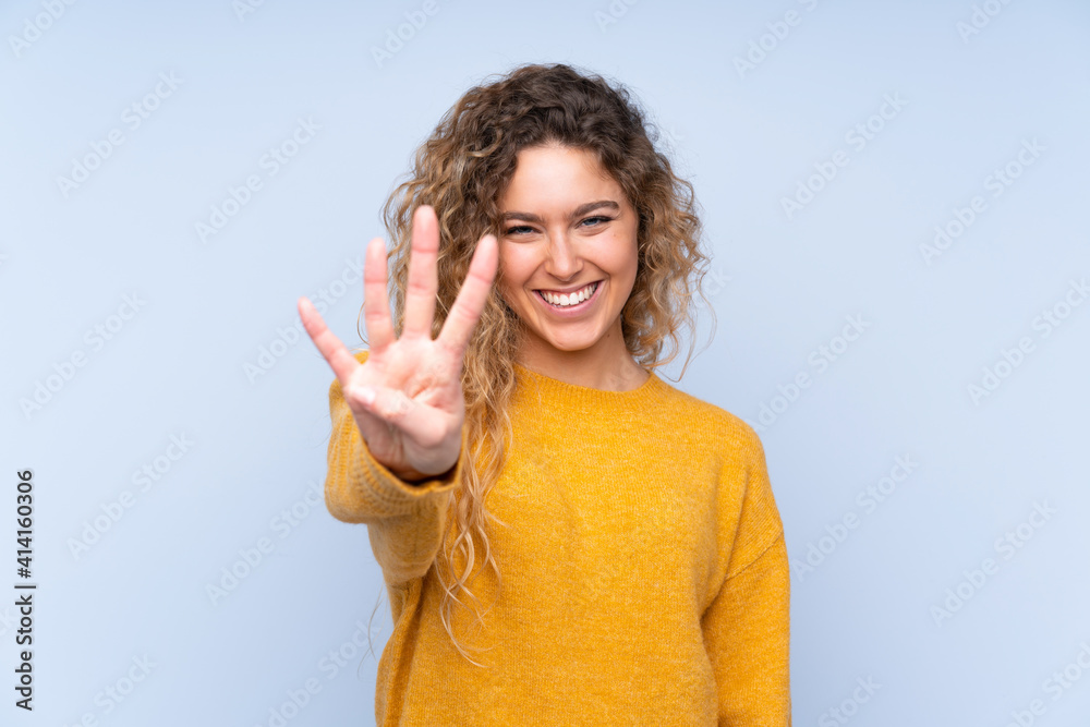 Young blonde woman with curly hair isolated on blue background happy and counting four with fingers