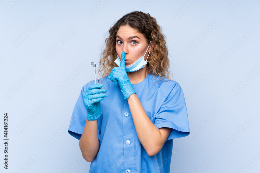 Young blonde woman dentist holding tools isolated on blue background doing silence gesture Young blonde woman dentist holding tools isolated on blue background doing silence gesture