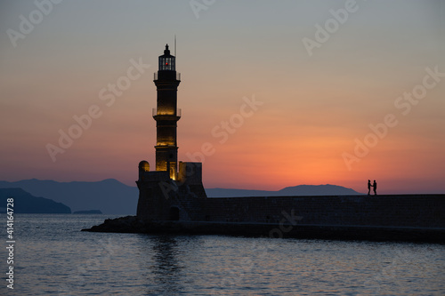 Couple watching sunset at Chania Lighthouse on Crete, Greece.