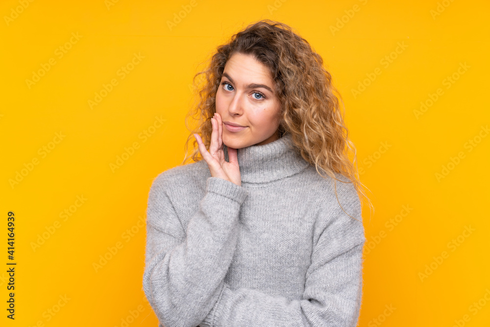 Young blonde woman with curly hair wearing a turtleneck sweater isolated on yellow background Looking front Young blonde woman with curly hair wearing a turtleneck sweater isolated on yellow background Looking front