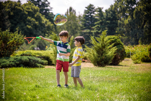 Boy blowing soap bubbles while an excited kid enjoys the bubbles. Happy teenage boy and his brother in a park enjoying making soap bubbles. Happy childhood friendship concept