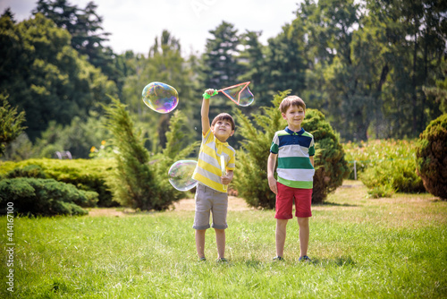 Boy blowing soap bubbles while an excited kid enjoys the bubbles. Happy teenage boy and his brother in a park enjoying making soap bubbles. Happy childhood friendship concept