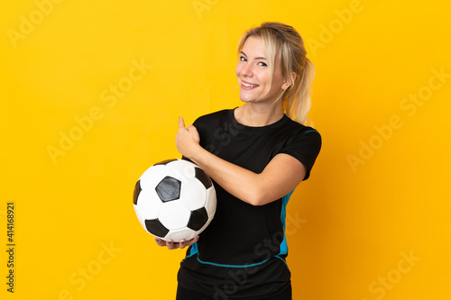 Young Russian football player woman isolated on yellow background pointing back © luismolinero