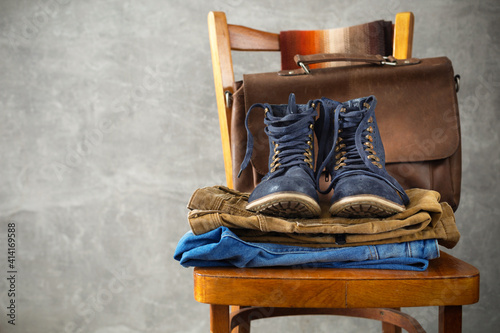 Denim jeans and old boots shoes with leather bag at old wooden chair