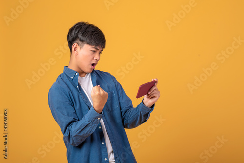 Young Asian man is watching his phone with happy and enjoy on an orange background.