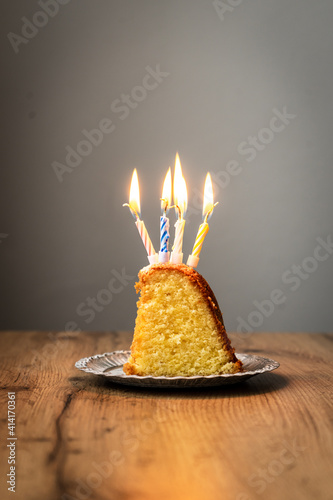 Ein St  ck Kuchen mit brennenden Geburtstagskerzen auf einem Teller. Brauner Holz Tisch  feiern.