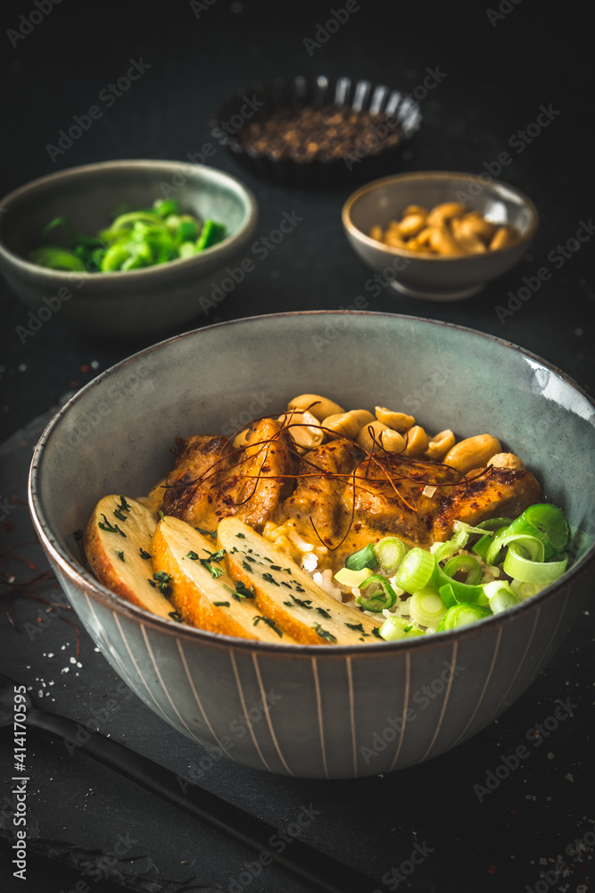 Buddha bowl with chicken, rice, peanuts, apple and chili sauce on dark background, vertical