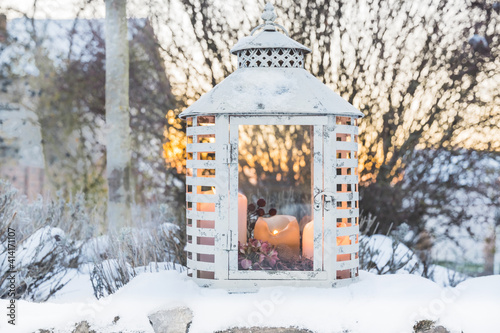 White vintage lantern with candles in a snowy garden in beautiful evening light