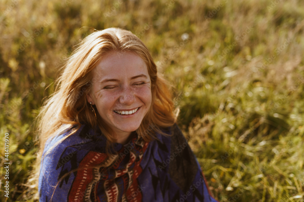 among the yellowed grass sits a girl with wheat hair and freckles on her face laughing joyfully with her eyes closed. High quality photo