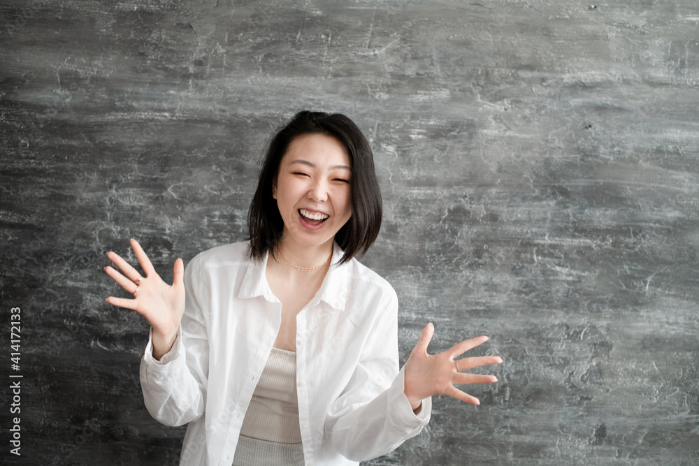 Happy, joyful, emotional Asian girl with spread fingers and white blouse against the background of a gray school board. Copy space. Back to school. Happy, joyful, emotional Asian girl with spread fingers and white blouse against the background of a gray school board. Copy space. Back to school.
