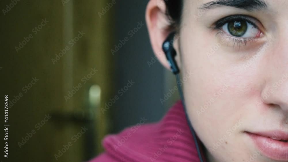 Detalle de una mujer joven poniéndose unos auriculares para escuchar música. Se ve medio rostro, ojos verdes.