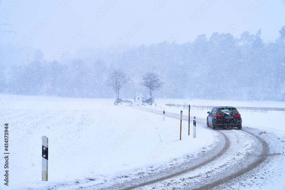 Auto auf Schneebedeckter kurviger Straße bei Schneesturm im Winter mit Brücke und Wald am Horizont Auto auf Schneebedeckter kurviger Straße bei Schneesturm im Winter mit Brücke und Wald am Horizont