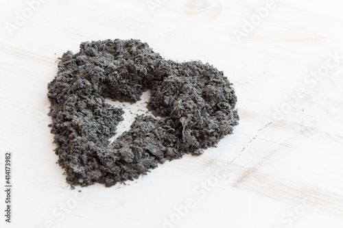 Cross in heart of ashes on white wood background with copy space photo