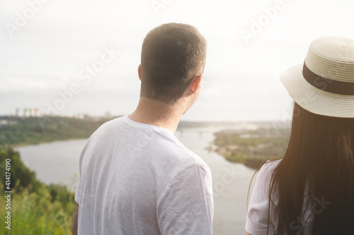 Behind people-a guy in a white T-shirt and a girl in a fashionable hat with dark long hair are walking in nature.