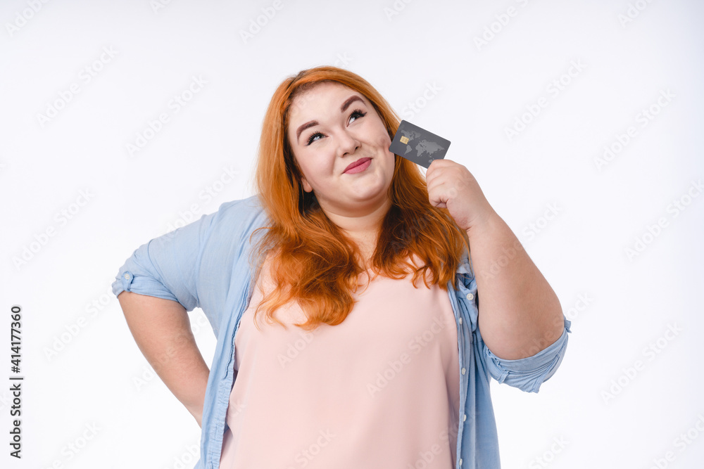 Pensive red-haired plump woman with credit card isolated in white background Pensive red-haired plump woman with credit card isolated in white background