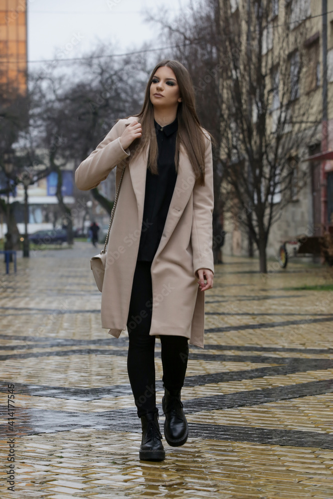 Outdoor portrait of young stylish woman in camel coat in the city on a rainy day