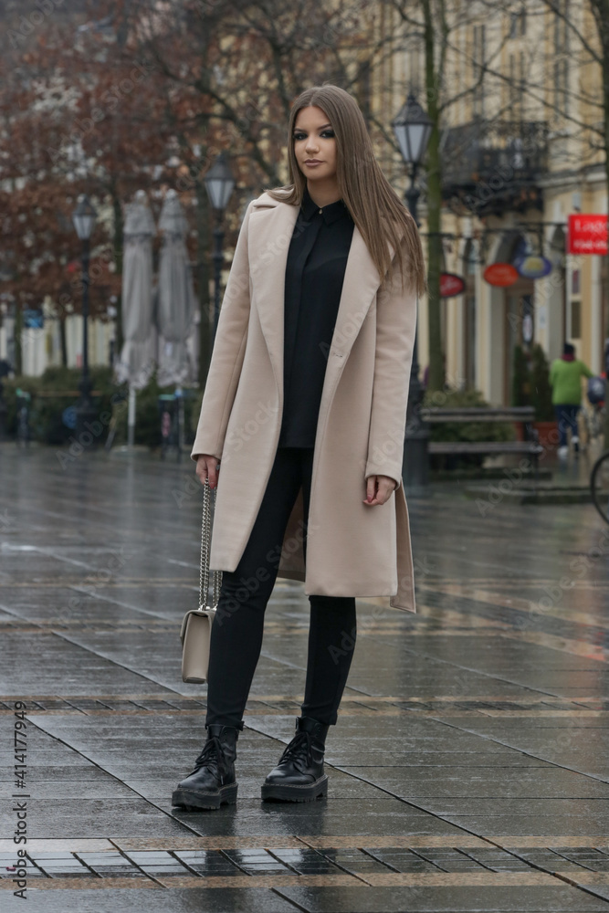 Outdoor portrait of young stylish woman in camel coat in the city on a rainy day