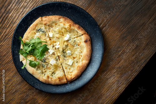 Wood-fired pizza with 4 types of cheese and white sauce with crispy sides, served on a black plate on a wooden background. pizzette a kind of Italian pizza