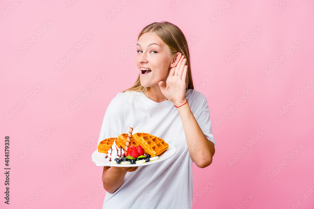 Young russian woman eating a waffle isolated trying to listening a gossip.