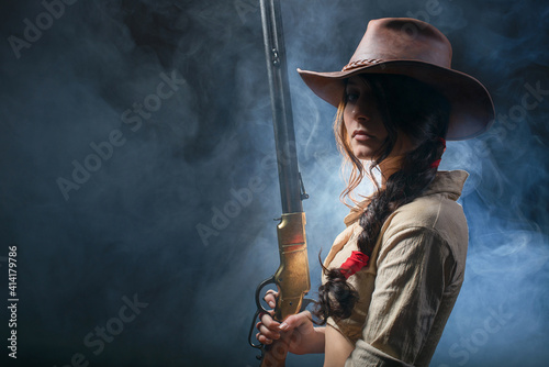 Canvas Portrait of a beautiful brunette cowgirl with a rifle on a background of smoke