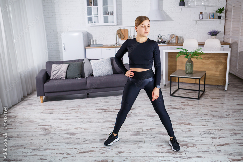 A young slender woman goes in for sports at home, wearing fitness clothes, a black top and leggings. Fitness at home for a beautiful body. Warm up before playing sports A young slender woman goes in for sports at home, wearing fitness clothes, a black top and leggings. Fitness at home for a beautiful body. Warm up before playing sports