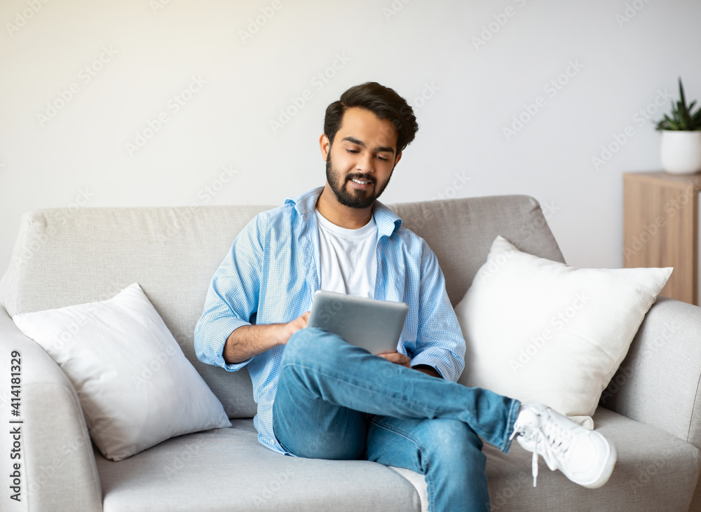 Modern Technologies For Leisure. Smiling Arab Man Using Digital Tablet At Home Modern Technologies For Leisure. Smiling Arab Man Using Digital Tablet At Home