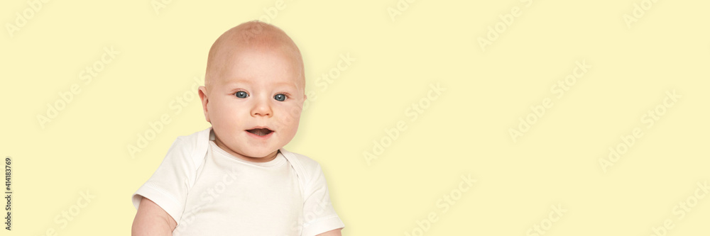 Cute small boy lying at bed. Childhood concept. Yellow background. Smiling child. Happy emotion. Copyspace. Stay home. Mockup. Horizontal banner. White clothes