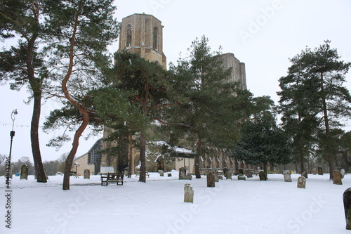 Snow scene landscape of historic ruin of Wymondham Abbey in Norfolk East Anglia England UK after icy cold blizzard heavy snowfall layer over graveyard and grave stones in Spring frozen weather	 photo