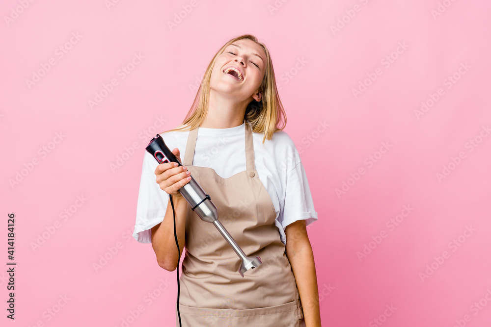 Young russian cook woman holding an electric mixer isolated relaxed and happy laughing, neck stretched showing teeth.