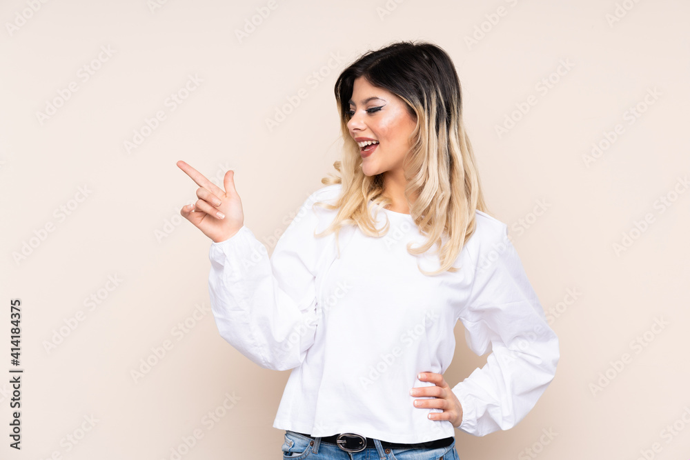 Teenager girl isolated on beige background pointing finger to the side and presenting a product Teenager girl isolated on beige background pointing finger to the side and presenting a product