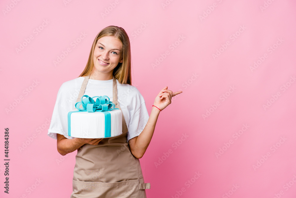 Young russian baker woman holding a delicious cake smiling and pointing aside, showing something at blank space. Young russian baker woman holding a delicious cake smiling and pointing aside, showing something at blank space.