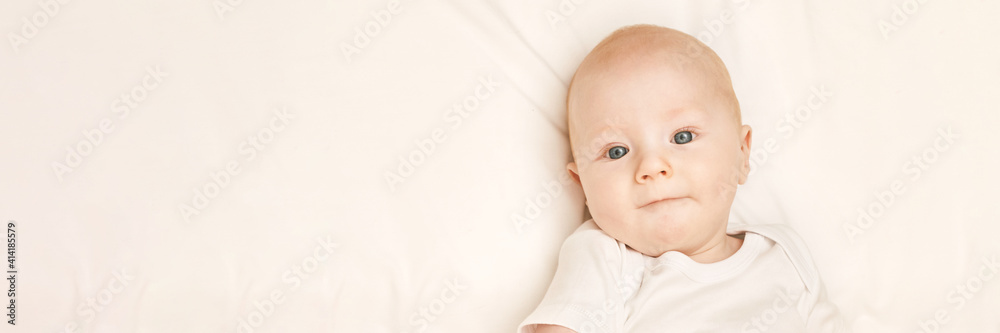 Cute small boy lying at bed. Childhood concept. Light background. Serious child. Copyspace. Stay home. Mockup. Horizontal banner. White clothes