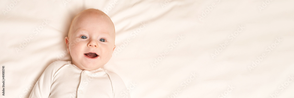 Cute small boy lying at bed. Childhood concept. Light background. Smiling child. Happy emotion. Copyspace. Stay home. Mockup. Horizontal banner