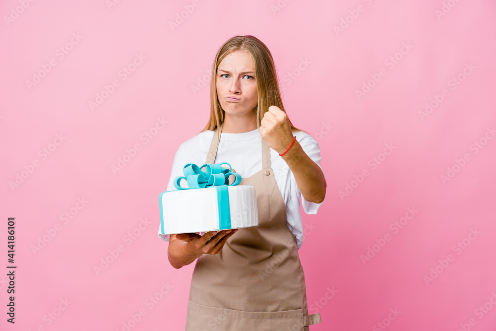 Young russian baker woman holding a delicious cake showing fist to camera, aggressive facial expression. Young russian baker woman holding a delicious cake showing fist to camera, aggressive facial expression.