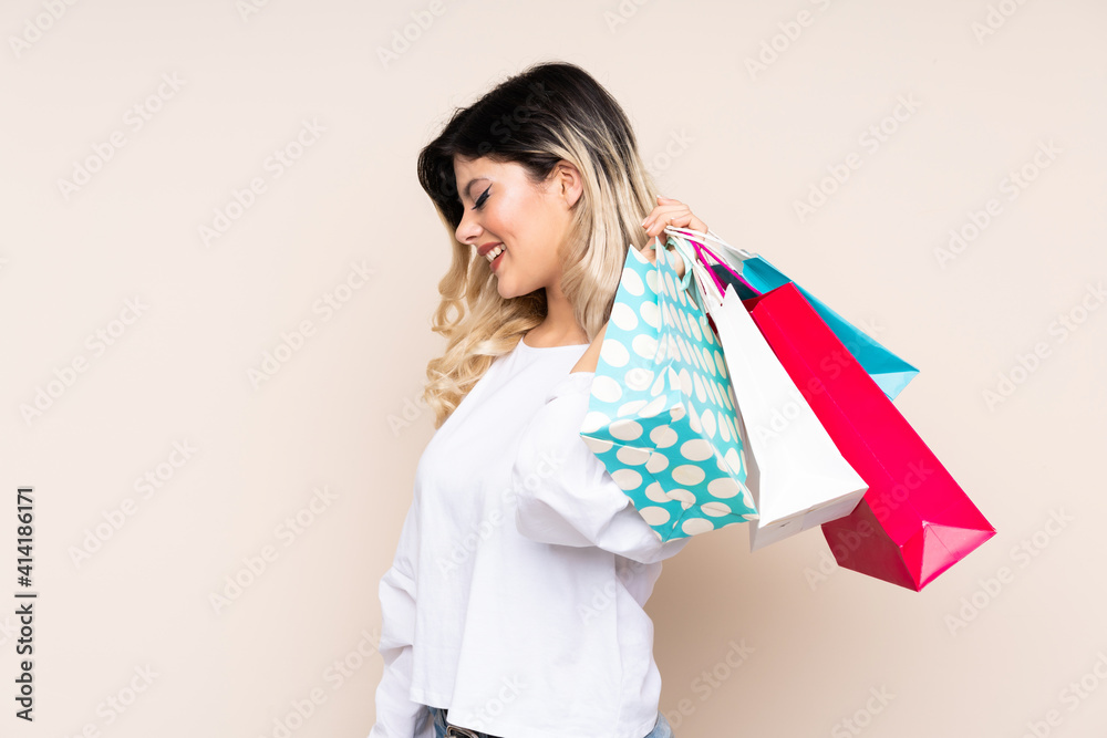 Teenager girl isolated on beige background holding shopping bags and smiling Teenager girl isolated on beige background holding shopping bags and smiling