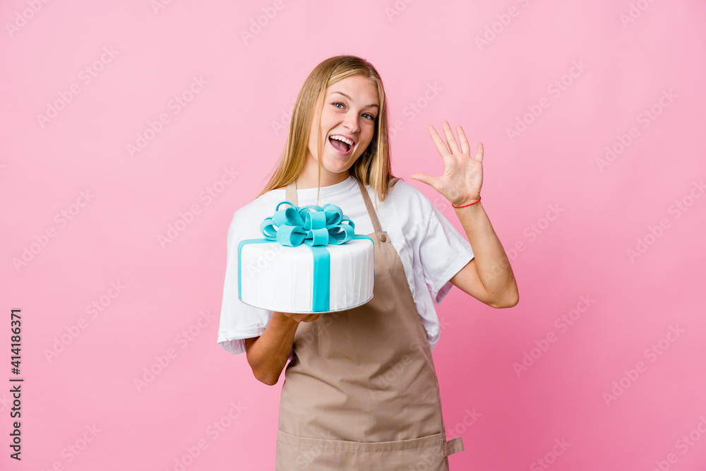 Young russian baker woman holding a delicious cake showing number ten with hands. Young russian baker woman holding a delicious cake showing number ten with hands.