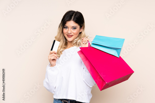 Teenager girl isolated on beige background holding shopping bags and a credit card