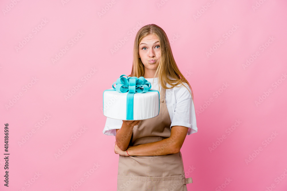 Young russian baker woman holding a delicious cake blows cheeks, has tired expression. Facial expression concept. Young russian baker woman holding a delicious cake blows cheeks, has tired expression. Facial expression concept.