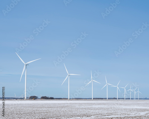 snow covered fields and wind turbines in dutch polder of flevoland under blue sky