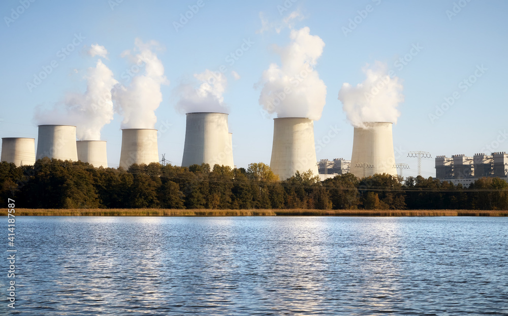 Power plant with smoking chimneys by a lake at sunset.